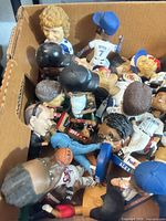 Box containing numerous resin sports bobbleheads in various uniforms