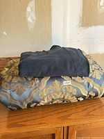 Folded comforter with black fleece blanket stacked on wooden surface