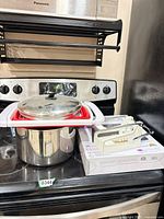 All items grouped on stove: stock pot with strainer on top, boxed hand press, lot sticker visible