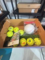 Box containing yellow softballs, stamp sheets, artificial turf, jumbo baseball in case