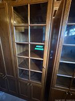 Front view of tall oak veneer display cabinet with glass-paneled upper door and wood lower doors