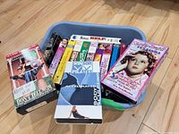 Blue tote containing multiple VHS tapes—visible titles include Don’t Tell Mom The Babysitter’s Dead, Beatles Help!, Winsor Pilates Accelerated Body Sculpting, Shirley Temple set plus other assorted tapes.