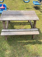 Full view of weathered gray solid wood picnic table with attached benches on lawn