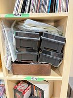 Stacked black plastic cassette trays and brown zippered case on shelf