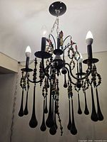 Full view of chandelier hanging, showing five bulbs, black frame, bead strands and teardrop drops