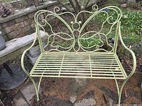 Full view of green wrought iron butterfly bench on patio