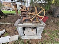 Overall view of cast iron stationary engine pump on wood base showing flywheel and pipe fittings