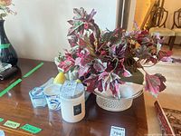 Tabletop view showing artificial foliage in white bowl planter, jar candles and votive candles