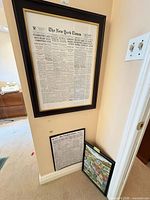 Large framed New York Times front page beside two smaller framed pieces leaning against wall