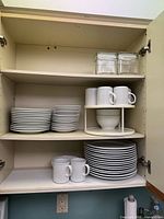 Cabinet view showing stacks of salad plates, mugs on turntable, bowls and dinner plates