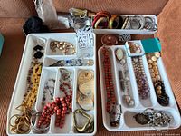 Overview of two white trays filled with assorted jewelry pieces