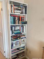 Tall white shelving unit filled with many paperback and hardcover books