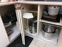 Cabinet view showing mixed bakeware, salad spinner, stock pots