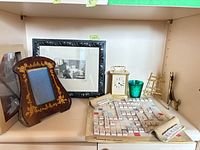 All items on shelf: framed print, wooden floral frame, brass carriage clock, green glass votive, brass easel, tile board