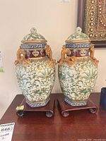 Front view of both lidded vases on stands