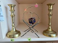 Pair of brass candlesticks flanking rotating dreidel ornament on shelf