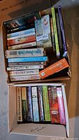 Two cartons filled with assorted paperback and hardcover books, spines visible