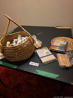 Basket of assorted acrylic paints, craft stick packs, wood panels and trivets on table