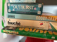 Stack of five board games showing Outburst, Booby-Trap, Touché, Obsession
