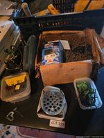 Assorted hardware on table including Bosch jigsaw, carton of nails, Tapcon box, drain cover, plastic bins