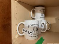 Three of the Jim's Excavating mugs stacked on shelf, logo visible