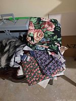 Stack of assorted fabrics and grey plastic sewing box