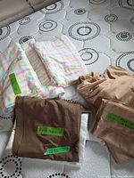 Three pastel plaid flannel sheets and taupe queen bedding pieces arranged on mattress