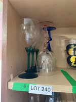 Shelf with multiple stemmed glasses: two wine glasses with green stems, several inverted glasses with blue and peach stems