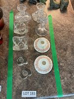 All eleven candle holders laid out within green tape: pressed glass stem pair at top, pressed glass block and heart styles in middle, porcelain floral pair at bottom