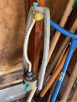 Oscillating lawn sprinkler hanging with garden tool handles visible