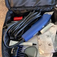 Open case showing blue corded clipper, lubricant tube, comb guard and accessories