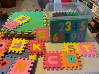 stack of large green and multicolour foam tiles, loose small letter tiles, clear bin holding additional tiles