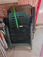 Stack of green plastic patio chairs with folded zero gravity chair behind