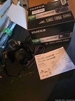 Camera with lens cap attached, strap visible, manual and box nearby