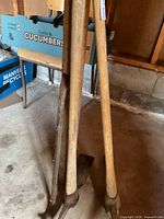Full view of three long wooden-handled pickaxes leaning against wall