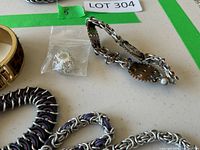 Top view of several bracelets including leopard bangle, steampunk gear bracelet, silver-purple chainmaille, and loose charm bead