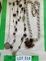 Three necklaces laid out: silver-tone chain with medallion, grey cord bead necklace, white seed-bead rope with bead cluster