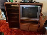 Front view of wood media stand showing glass door, open TV bay, and lower cabinet doors