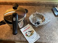 Pressure cooker assembled with lid, steamer basket, spare knob, manual visible