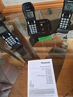 Full set on glass table showing three handsets, main base, instruction manual