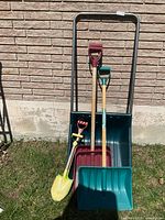 Group shot of sleigh shovel, three standard shovels and two child shovels against wall