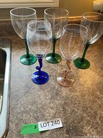 Five wine glasses with various colored stems on countertop