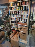 Tall shelving unit filled with multiple rows of vintage beer and soda cans; boxes of additional cans at base