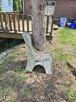 Concrete garden bench end leaning against tree, showing mounting slots and curved profile