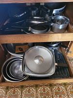 Cookware stacked in cabinet showing electric skillet base, grill pan, saucepans, mixing bowls