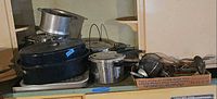 Cookware on shelf: stock pot, roaster with lid, pressure cooker, baking sheet underneath
