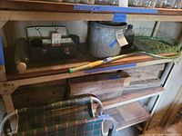 Shelf with tackle box, galvanized bucket, floater pole, landing net, plaid cot visible