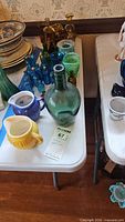 Overview of lot showing green demijohn, ceramic creamers, multiple blue bottles