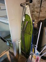 folded ironing board, dustpan, broom/mop handles, bucket with packaged cover