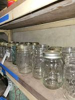 Row of clear pint mason jars with metal lids on shelf